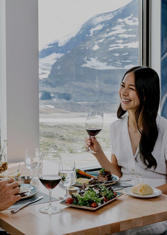 Couple being served dinner by large windows overlooking a mountain landscape.