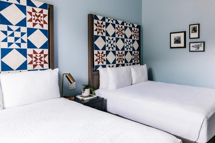 Two beds with red and blue quilted headboards, with artwork on the wall alongside.