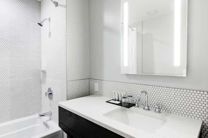 A sink and shower with white tiles and countertops.
