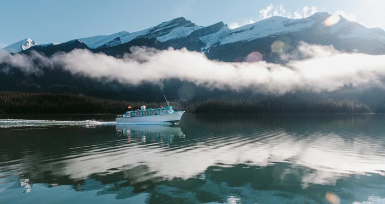 A boat glides along a mountain lake under light mist