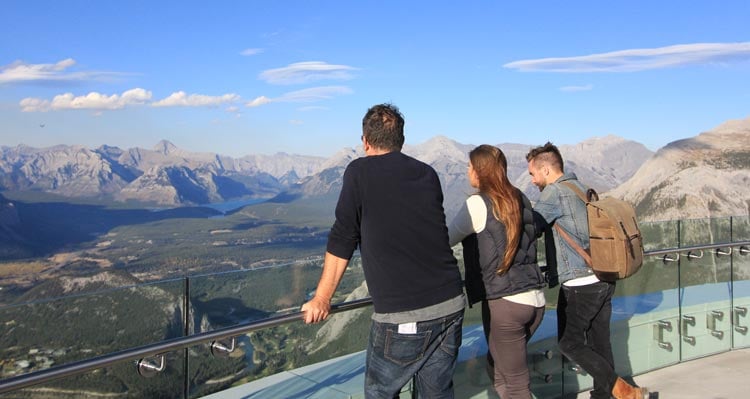 Three people look out at a wide valley and mountains from the top of the Banff Gondola.