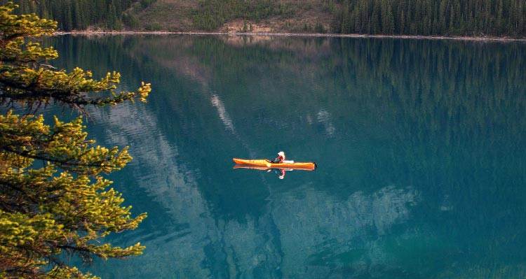 A kayaker paddles on a calm blue lake.