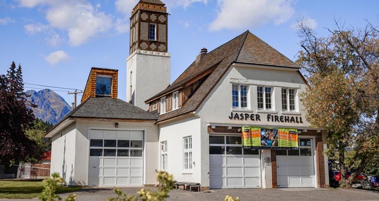 A historic firehall with a tower and garages with a half-hip roof.
