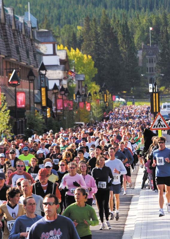 A crowd of runners race down a town street with forests behind. 