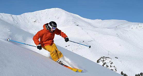 A skiier in red and yellow speeds down a snowy mountainside