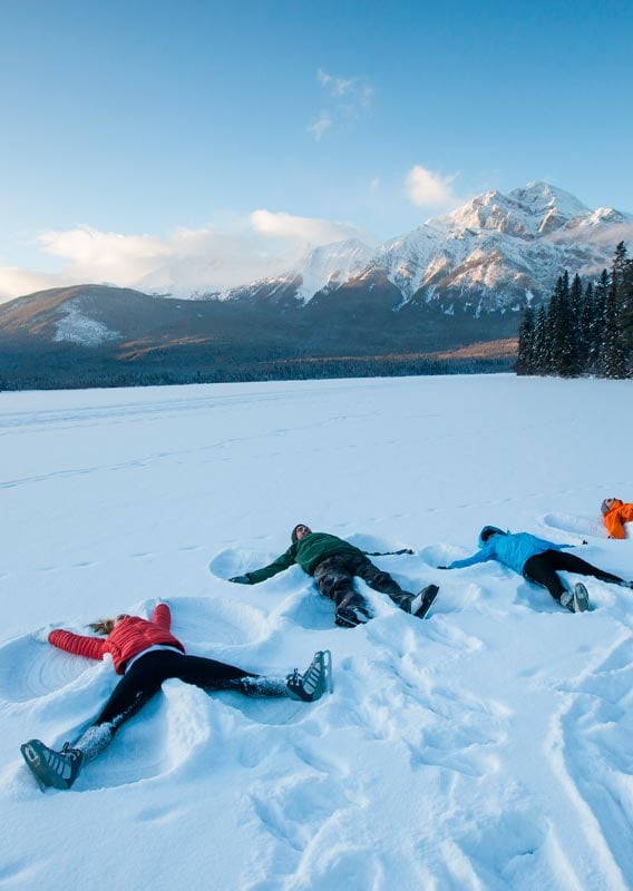 A group of people lay in the snow in front of a snow-covered mountain.