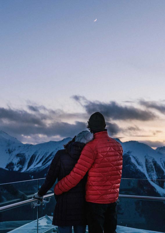A couple lean on each other at the top of Banff Gondola in winter at twilight