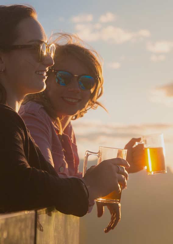 Woman stands overlooking mountain views holding a beer in the golden light of sunset