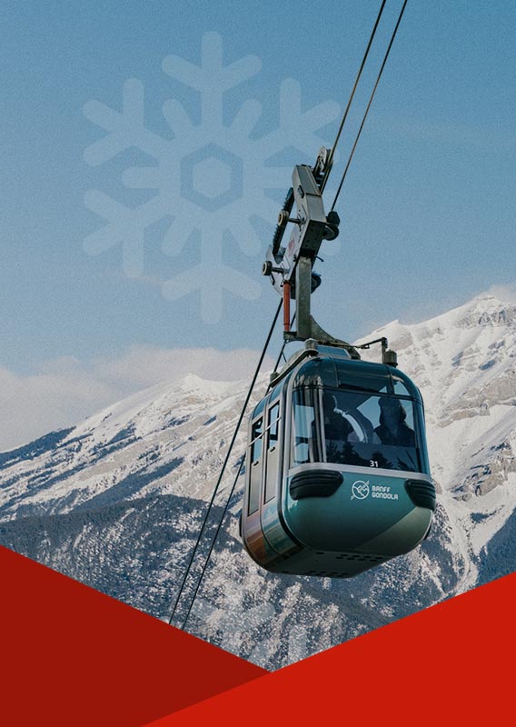 A gondola cabin rising above a valley and in front of snow-covered mountains.