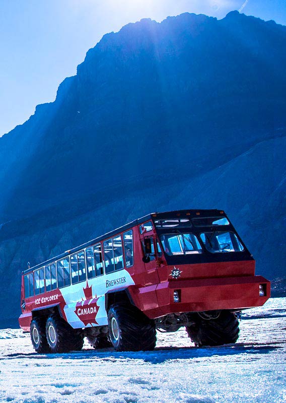 A red and white bus beneath mountains on a field of ice