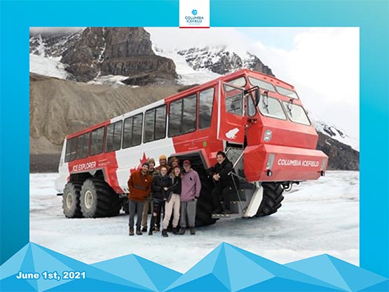 A group of people stand for a photo outside a large red and white glacier bus.