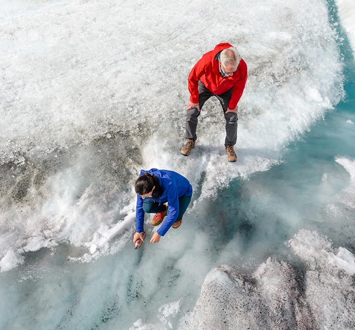 Two people stand at a stream running over a glacier.