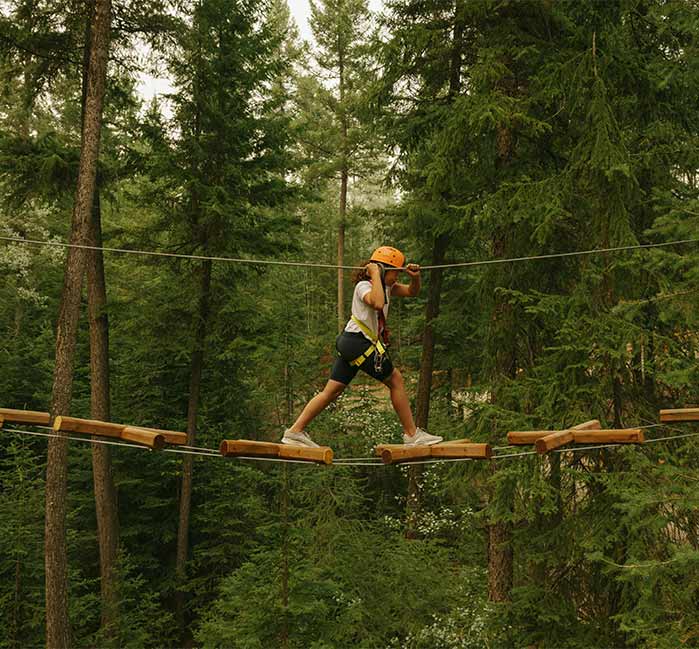 A child making their way through a suspended ropes course in the trees.