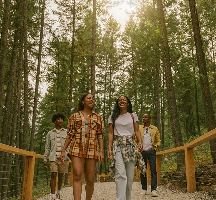 Four young friends walk through the trees on a gravel pathway in summer.