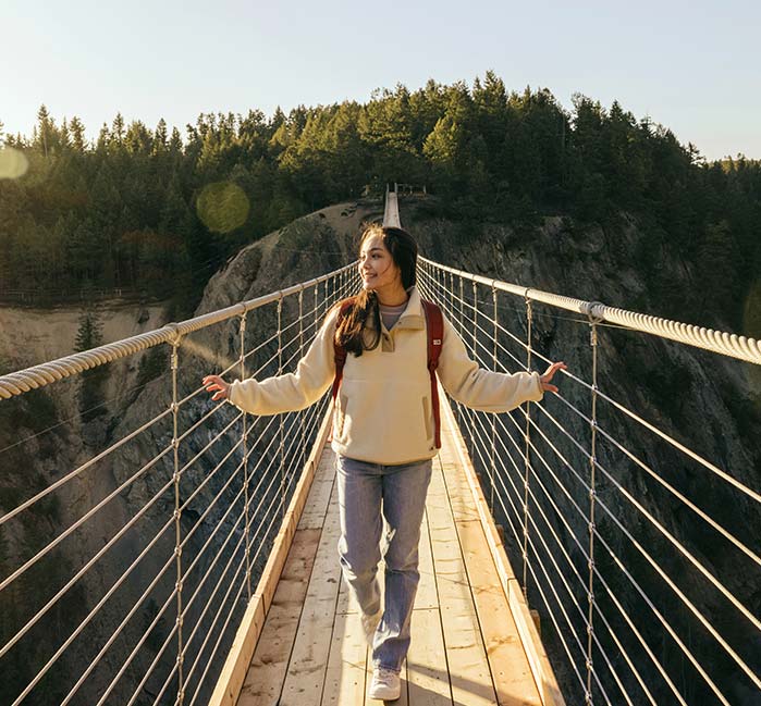 A person walks towards the camera on a narrow wooden suspension bridge.