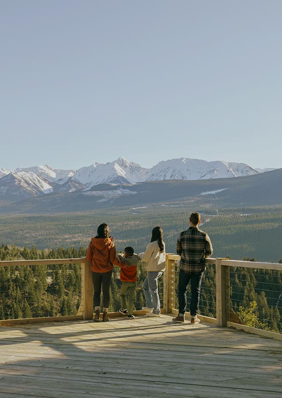 A family stands at a wooden platform, looking out over a wide valley.