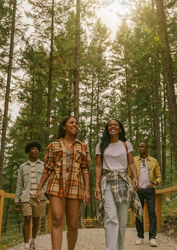 Four young friends walk towards the camera on a gravel path surrounded by trees.