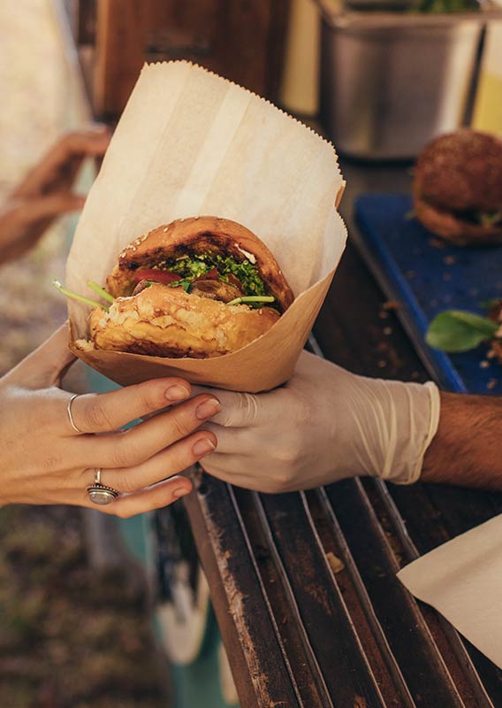 A burger is passed from a vendor to a woman, showing only their hands.