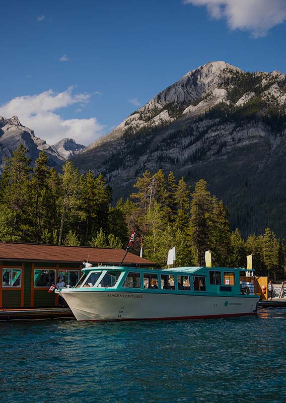 A tour boar at a dock on a lake below a forested mountain.