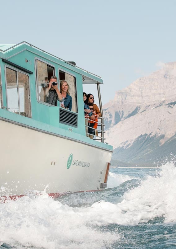 Groups of people look out from a boat as it makes a wave on a lake