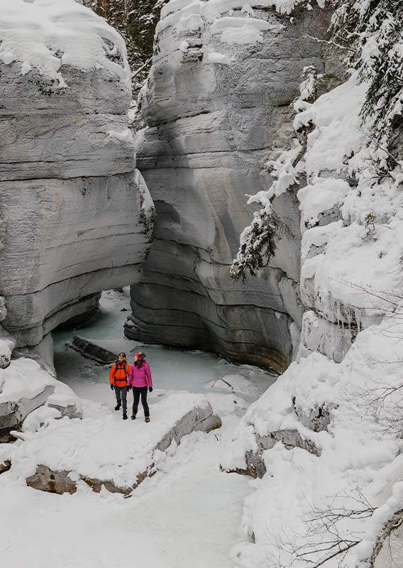Two people stand at the bottom of an ice canyon in the snow