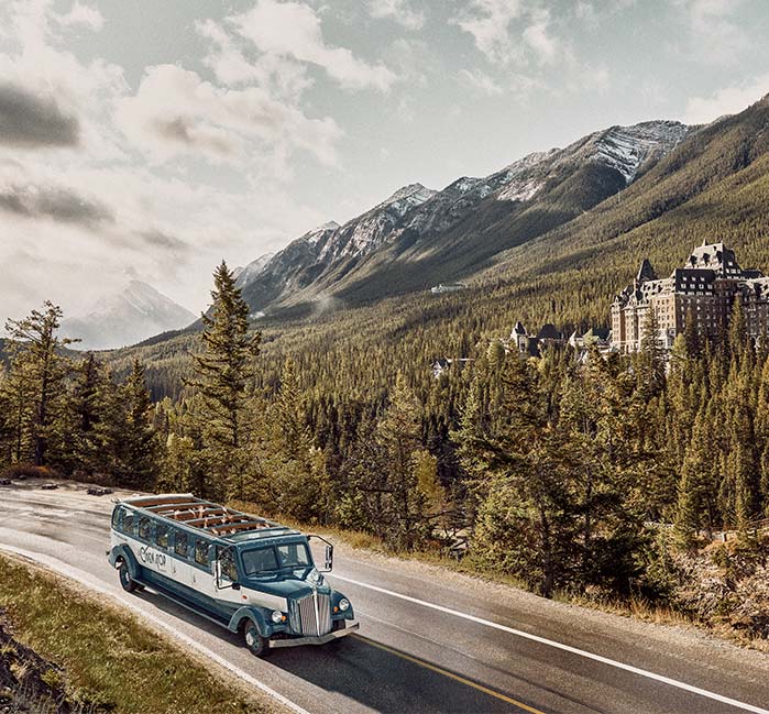 Tour bus driving past a historic hotel with mountains behind it.