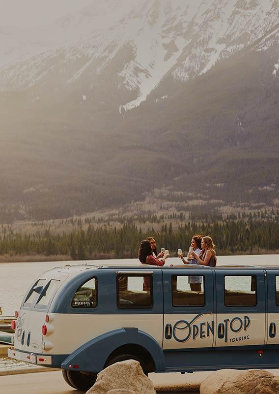 Tour bus parked next to a waterfront with guests cheering drinks standing through the open-top roof.