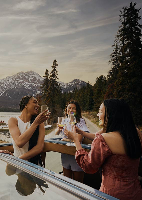 Three women toast drinks standing through open-top roof of vehicle.