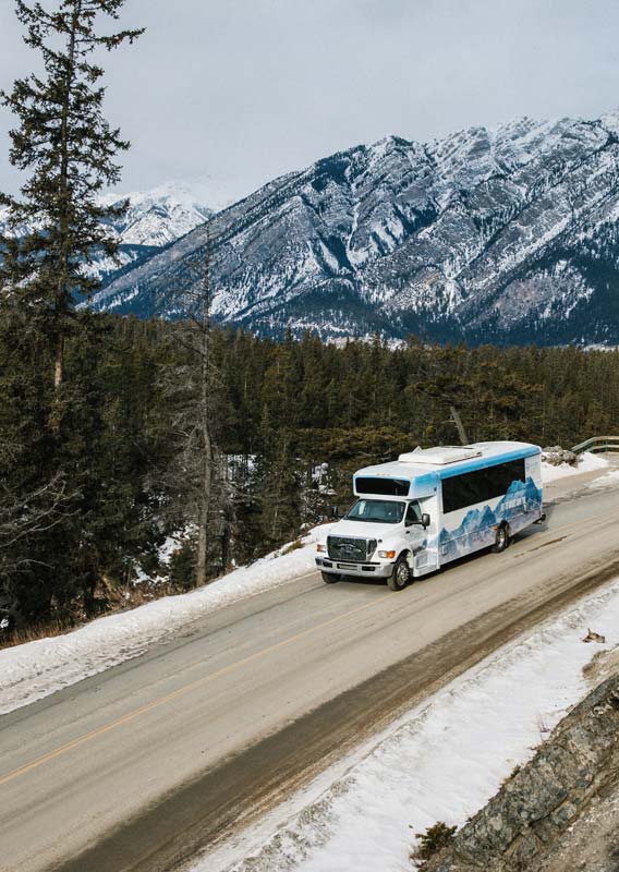 Brewster Express bus drives along a road beneath a snowy hillside