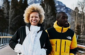 Two people in winter coats on a small pedestrian bridge.