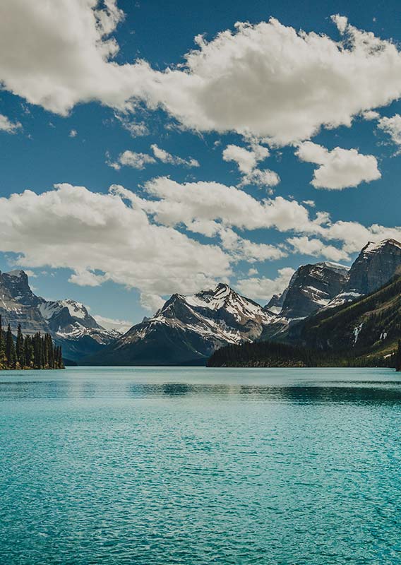 A calm blue lake below tall snow-covered mountains.