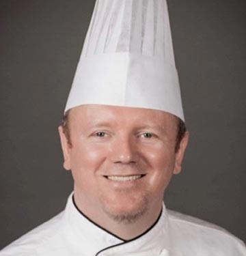 A chef stands against a grey background.