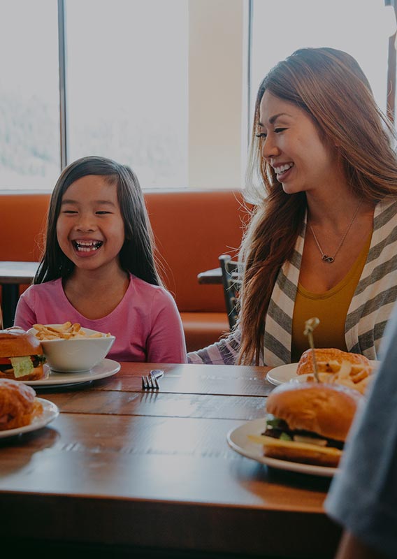 A family sit together at a dinner table to eat hamburgers.