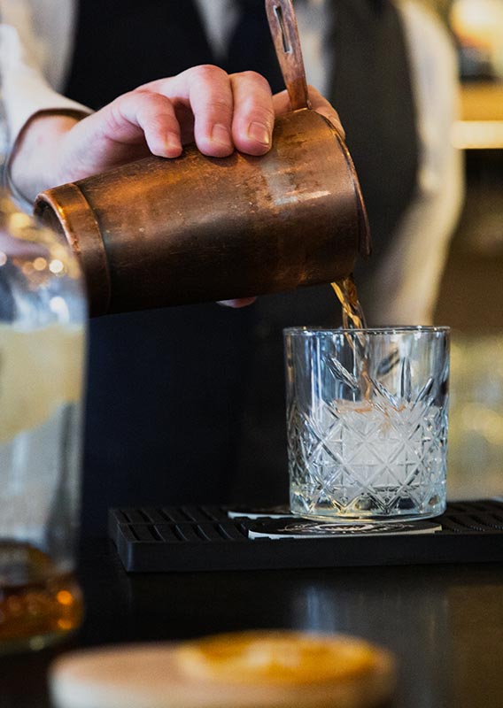 A bartender pours a cocktail from a shaker into a glass with ice.