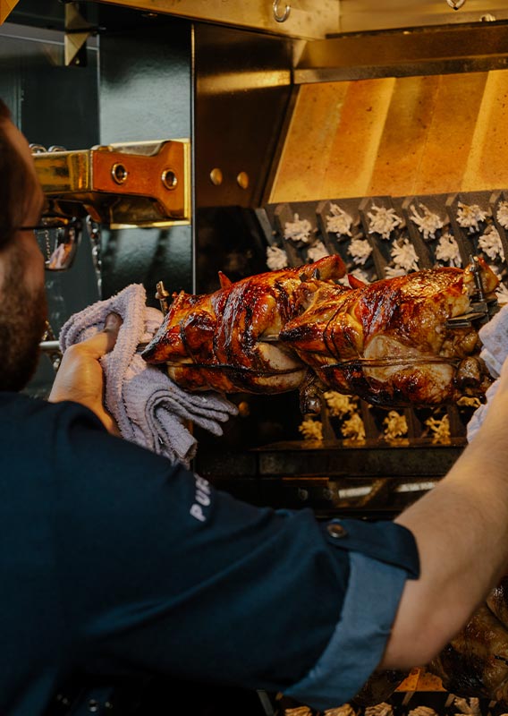 A kitchen cook takes rotisserie chickens out of an oven.