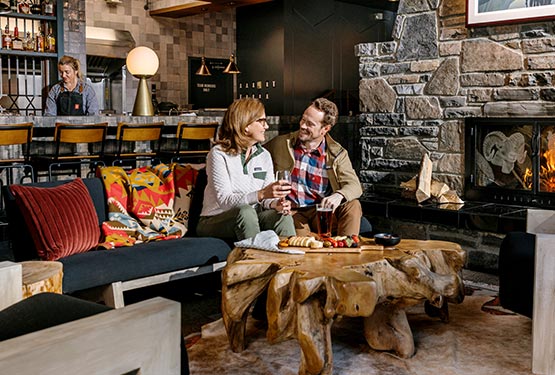 Two friends sit in a restaurant lounge by a fireplace.