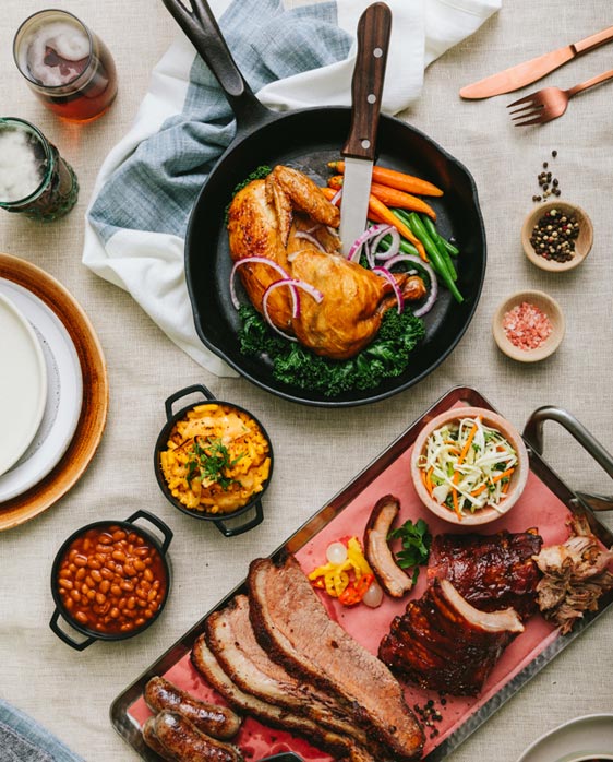 Family Style BBQ dinner spread viewed from above, featuring roast chicken, brisket, sausage, beans and more