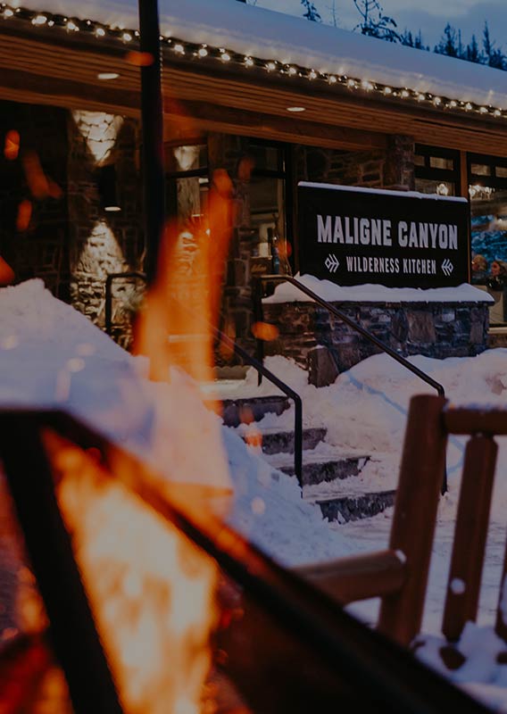 An outdoor firepit with the exterior of Maligne Canyon Wilderness kitchen is in the background