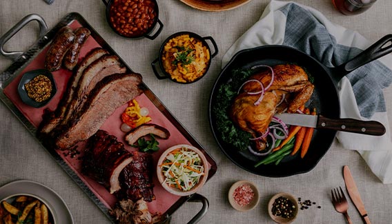 Family Style BBQ dinner spread viewed from above, featuring roast chicken, brisket, sausage, beans a