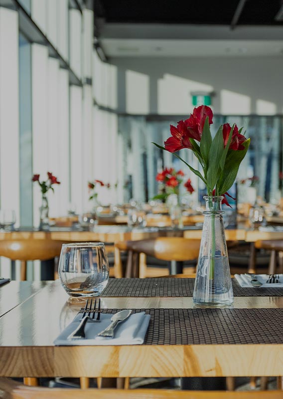 A restaurant table set with red flowers in the centre.