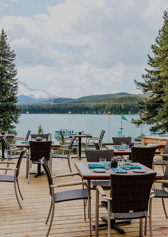Dining tables set up on a wooden patio looking over a lake surrounded by conifer trees