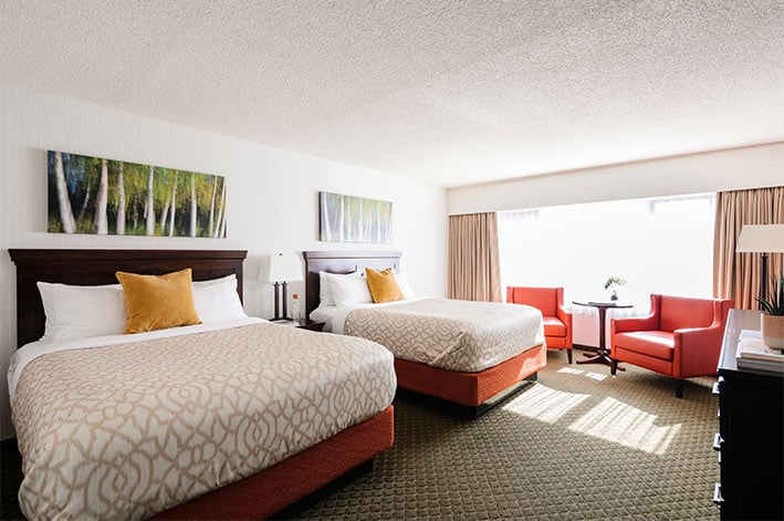 A hotel room with two beds, artwork and dresser