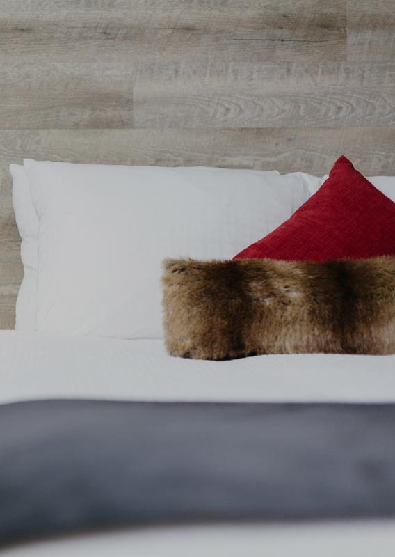 A hotel bed with side table decorated with pinecones and a lantern