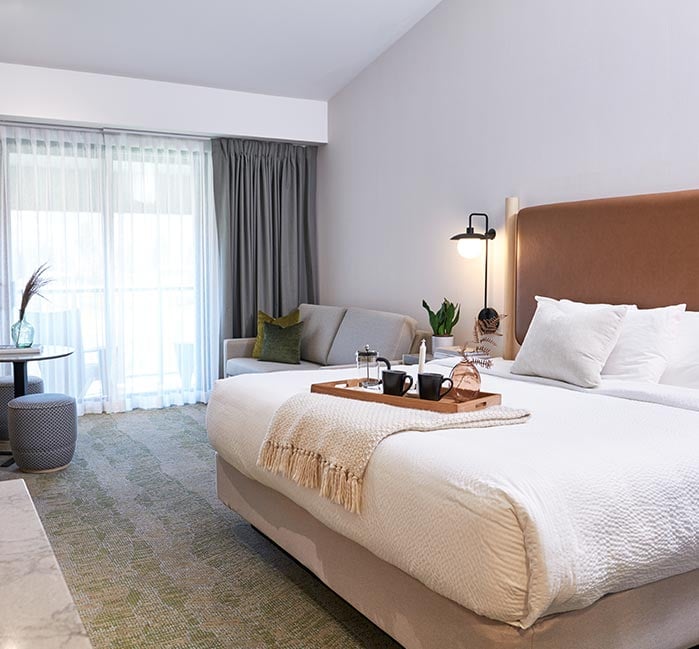 A hotel bed with a breakfast tray placed on a blanket.