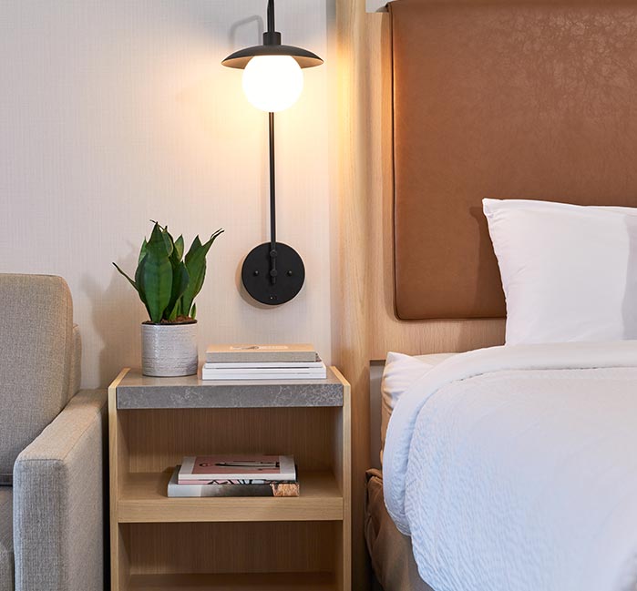 A bedside table between a hotel bed and sofa.