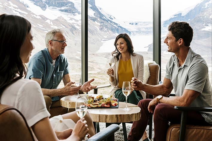 Four people sit around a wooden table with an appetizer board and glasses of wine.