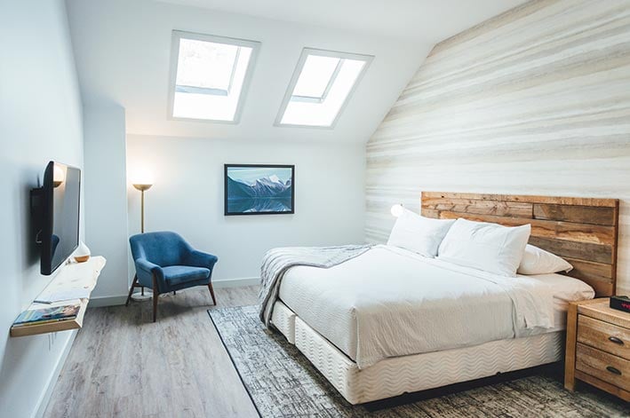A king bed in a room with an angled ceiling with a window looking out towards mountains.