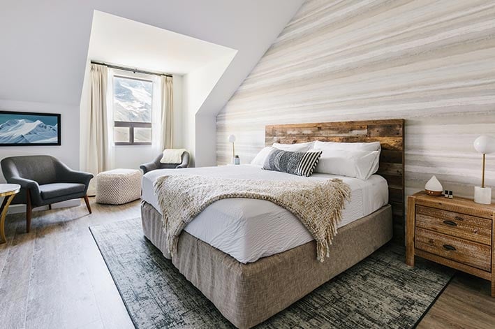 A king bed in a room with an angled ceiling with a window looking out towards mountains.