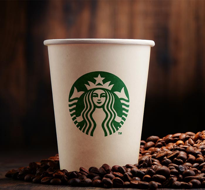 A Starbucks white cup surrounded by coffee beans on a table.