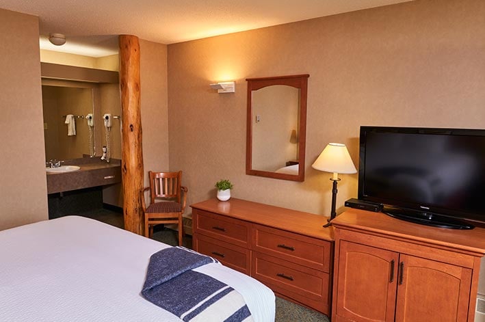 A king bed in a hotel room with view of cabinet, TV and bathroom entrance